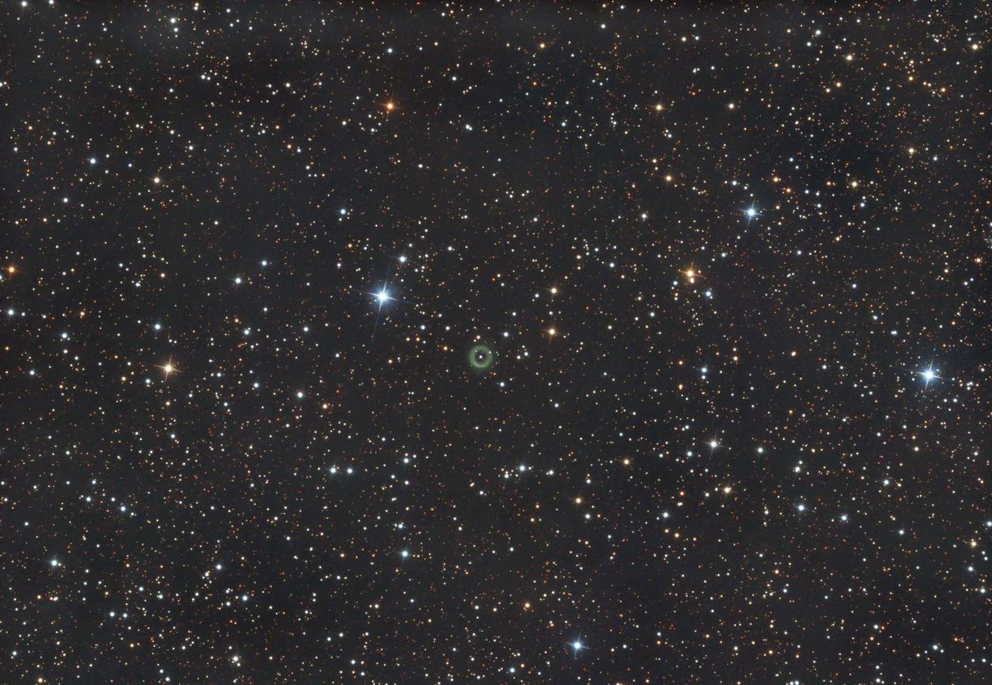 A dense star field with a small green ring-shaped nebula at the centre